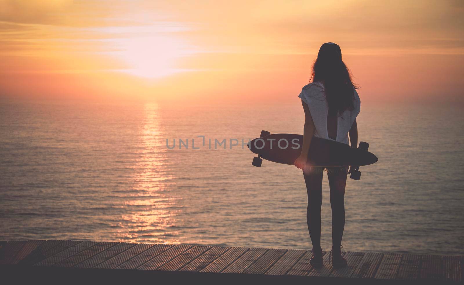 Beautiful girl with a skateboard looking to the sunset