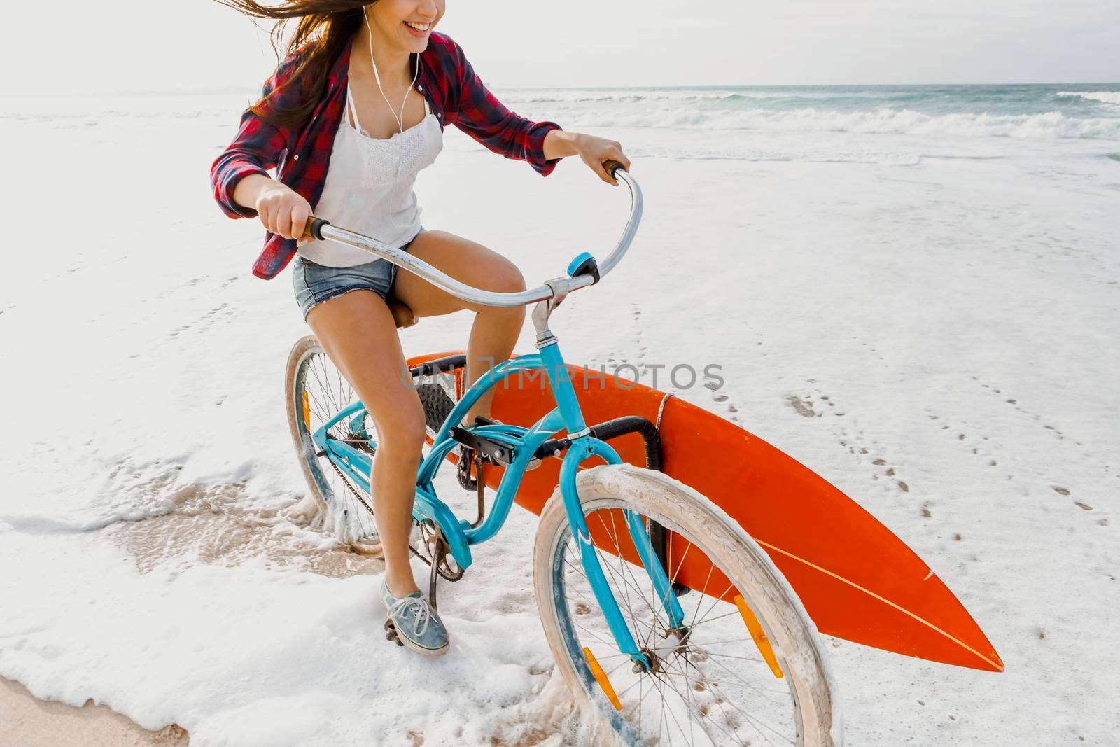 Surfer young woman riding her bicycle on the beach