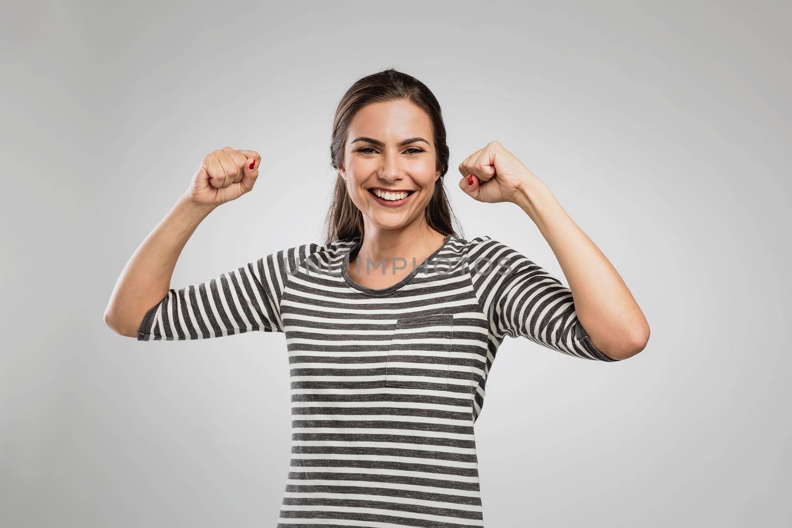 Beautiful happy woman with arms up over a gray background