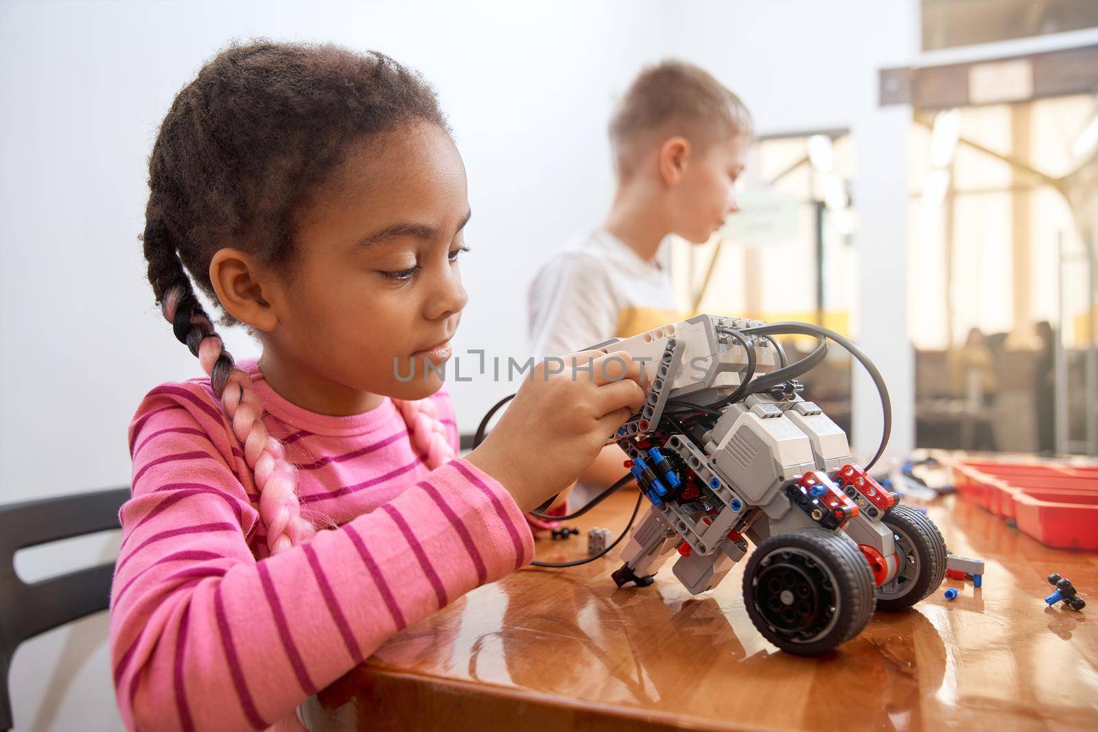 Building kit with colorful pieces for group of multiracial kids creating toys. Close up of concentrated african girl working on project, having positive emotions.. Concept of science engineering.