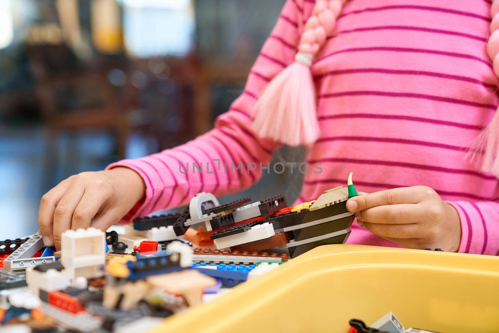 Front view of building kit for kids creating toys, having positive emotions and joy. Crop of incognito african girl working on project, hands taking colorful parts. Concept of science engineering.