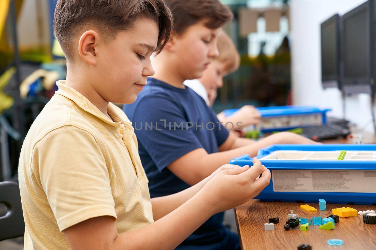 Interesting building kit for kids on table with computers. Side view of boys creating toys. Science engineering. Nice interested friends chatting and working on project together.