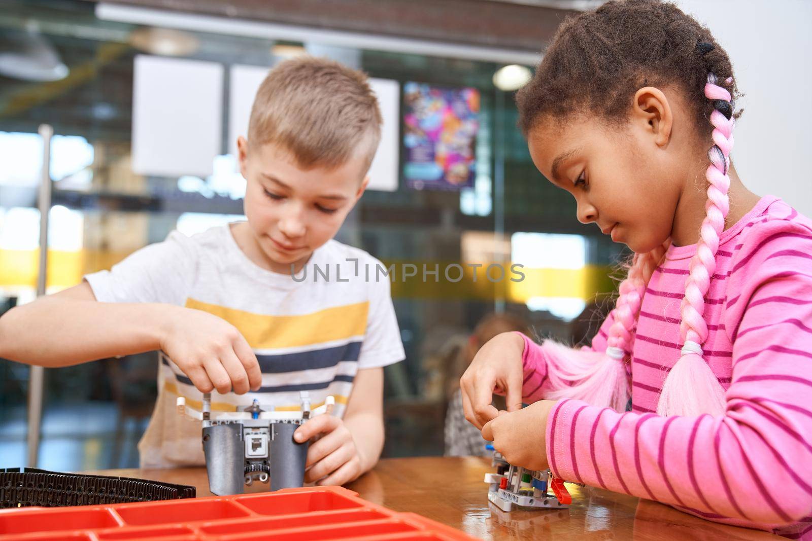 Building kit for group of multiracial kids creating toys. Close up of concentrated african girl and caucasian boy working on project, having positive emotions. Concept of science engineering.