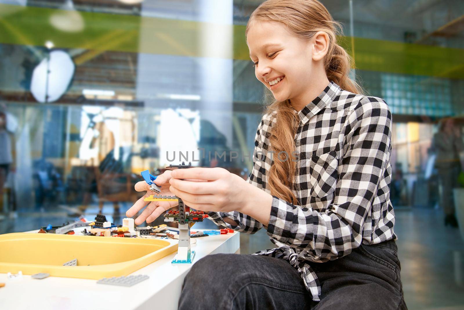Selective focus of lovely smiling caucasian girl working on project, using colorful parts and having positive emotions and joy. Building kit for toys creating. Concept of science engineering.
