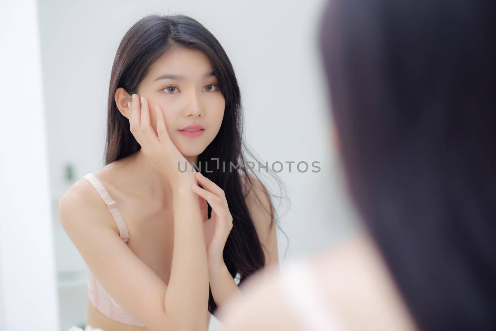 Beautiful young asian woman smiling look at mirror of checking face with skin care and cosmetic for rejuvenation and hygiene, beauty girl happy clean facial with cream or lotion and for health.