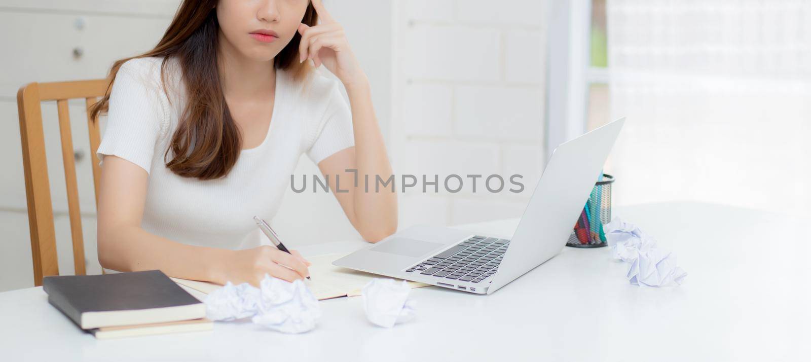 Young asian woman working with laptop computer think idea project and paper crumpled having problem on table at home, girl using notebook with frustrated and trouble, business and freelance concept.