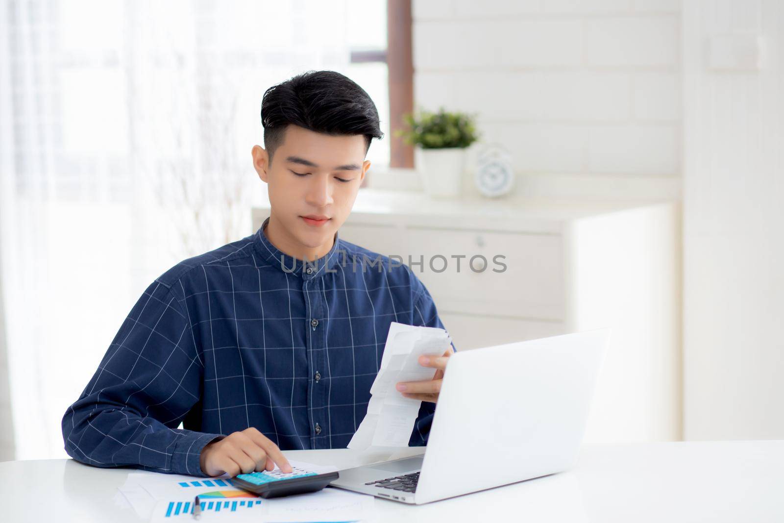 Young asian man calculating finance household with calculator on desk at home, male checking bill and success for saving expenses household, debt closure, tax and accounting, business concept.