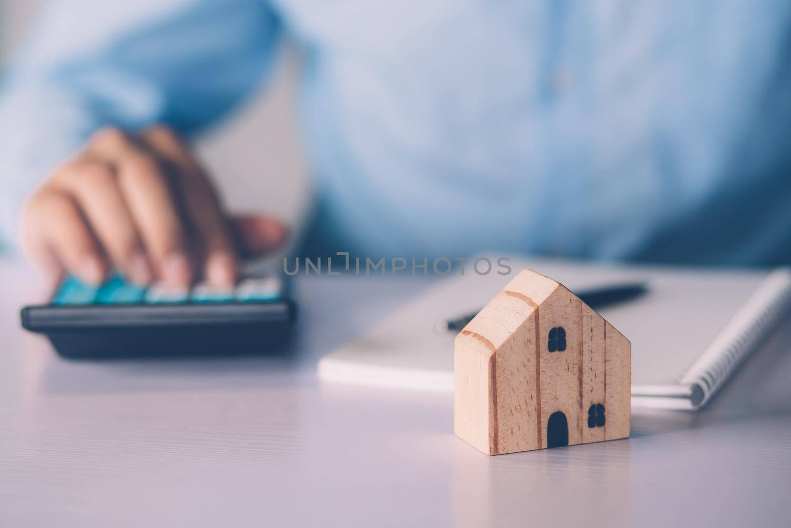 Hand of businessman planning and calculate expense and mortgage with calculator and home on desk, insurance and budget of residential, examining of loan and residence, business and property concept.