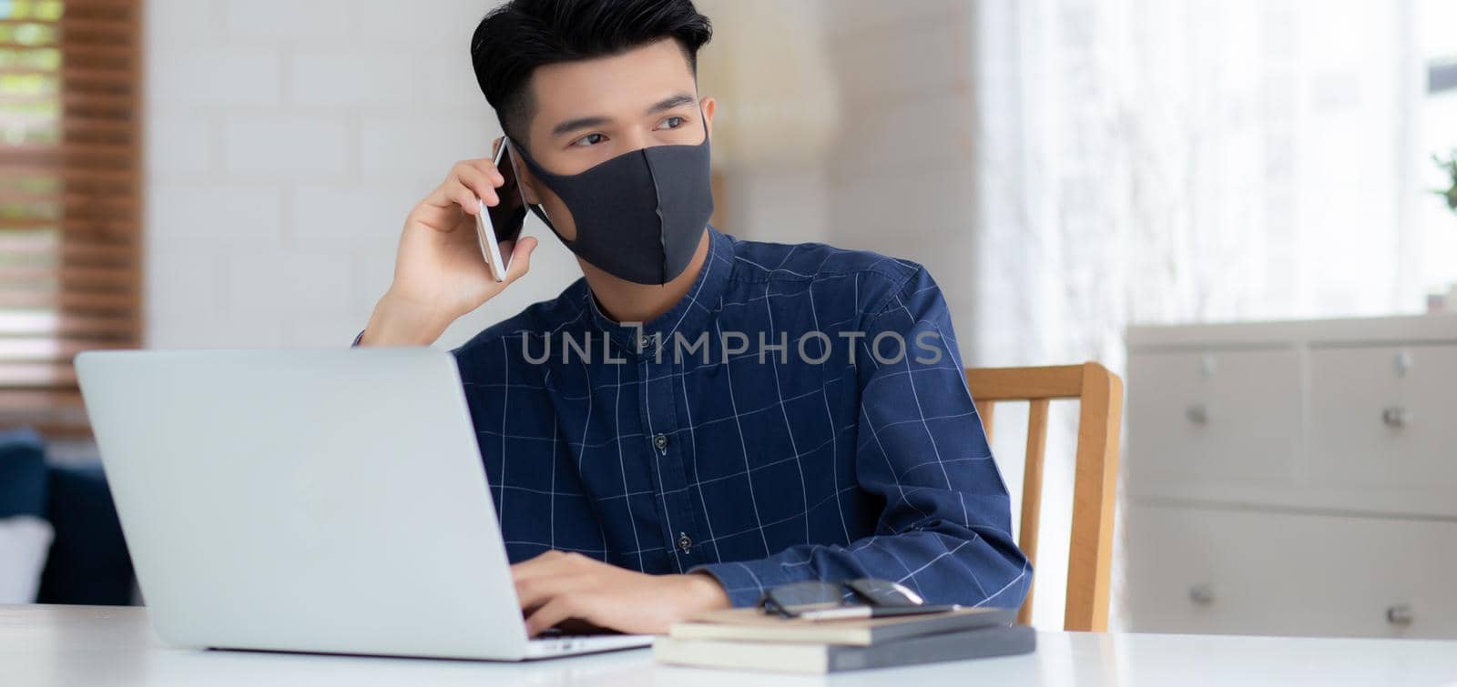Young asian business man in face mask talking smartphone and work on laptop computer for protect covid-19, businessman quarantine work from home with notebook, social distancing and stay home.