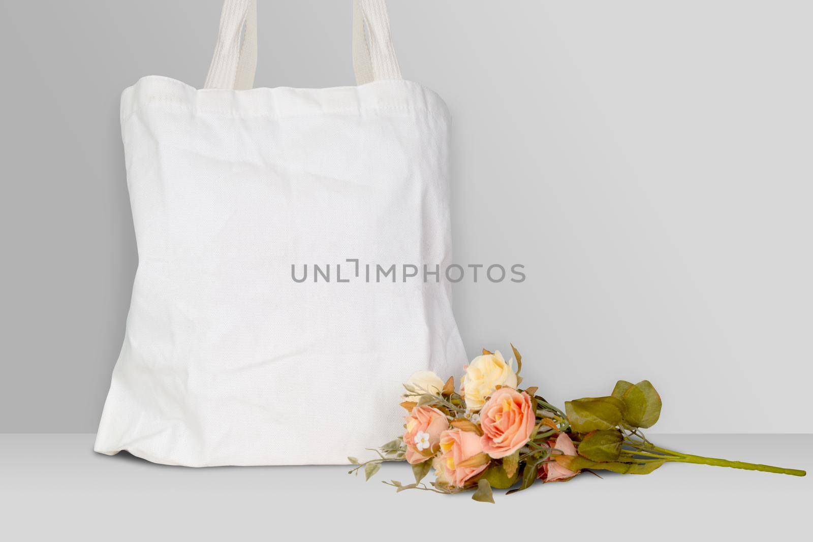 Mockup white tote bag fabric for shopping and flower on desk, mock up canvas bag textile with reusable.
