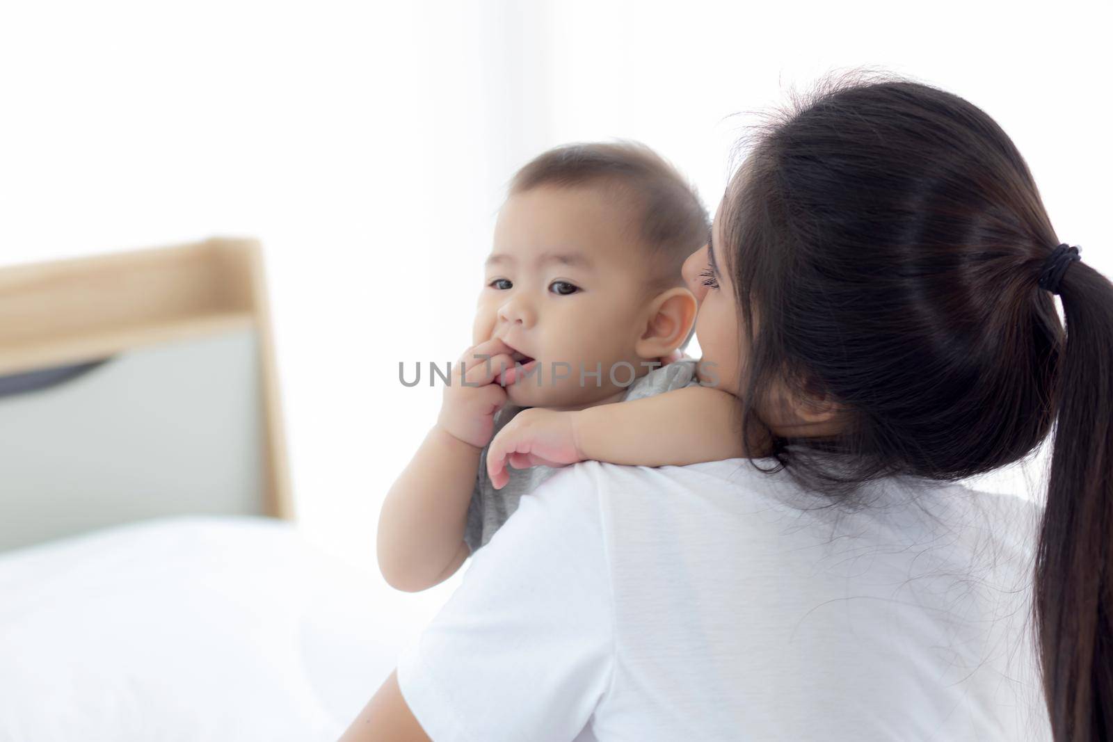 Young asian mother holding little baby girl together in the bedroom at home, mom carry child and care, woman and kid with carefree, toddler and parent, emotion and expression, family concept.