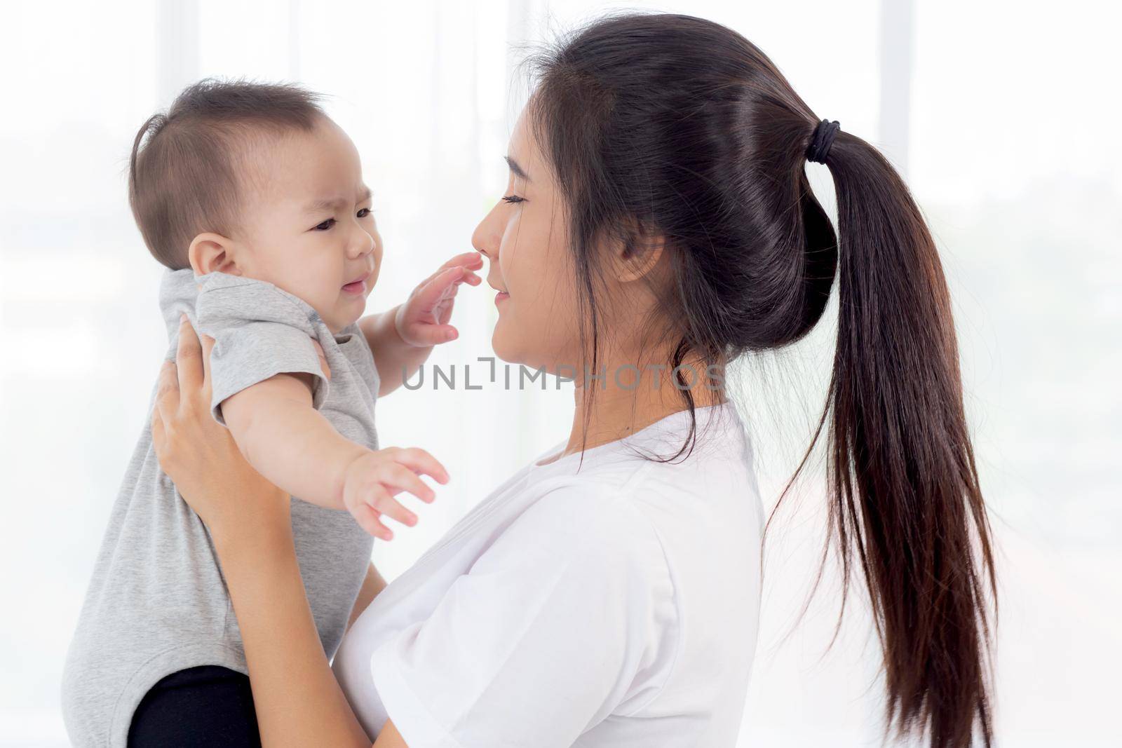 Young asian mother holding little baby girl together in the bedroom at home, mom carry child and care, woman and kid with carefree, toddler and parent, emotion and expression, family concept.