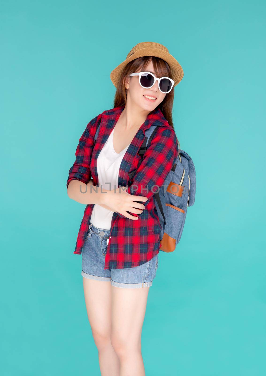 Beautiful portrait young asian woman wear sunglasses and hat smile excited and confident enjoy summer holiday isolated blue background, model girl cheerful having backpack in vacation, travel concept.