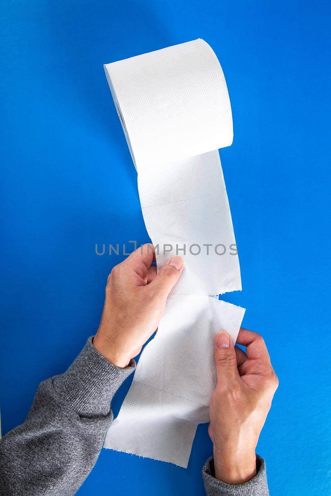 The hand tearing a piece of toilet roll, on the blue background