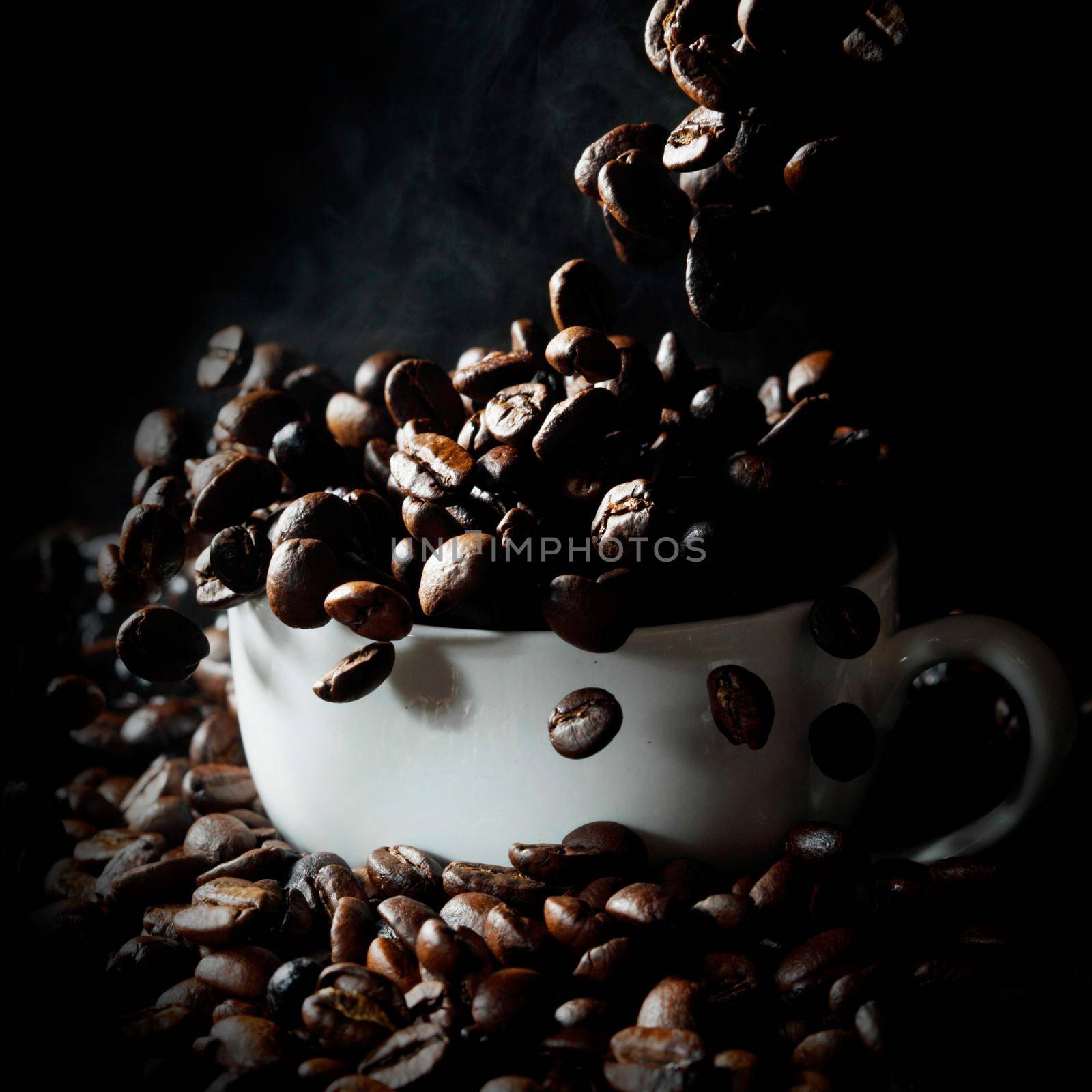 Cup filled with falling hot fresh steaming coffee beans on black