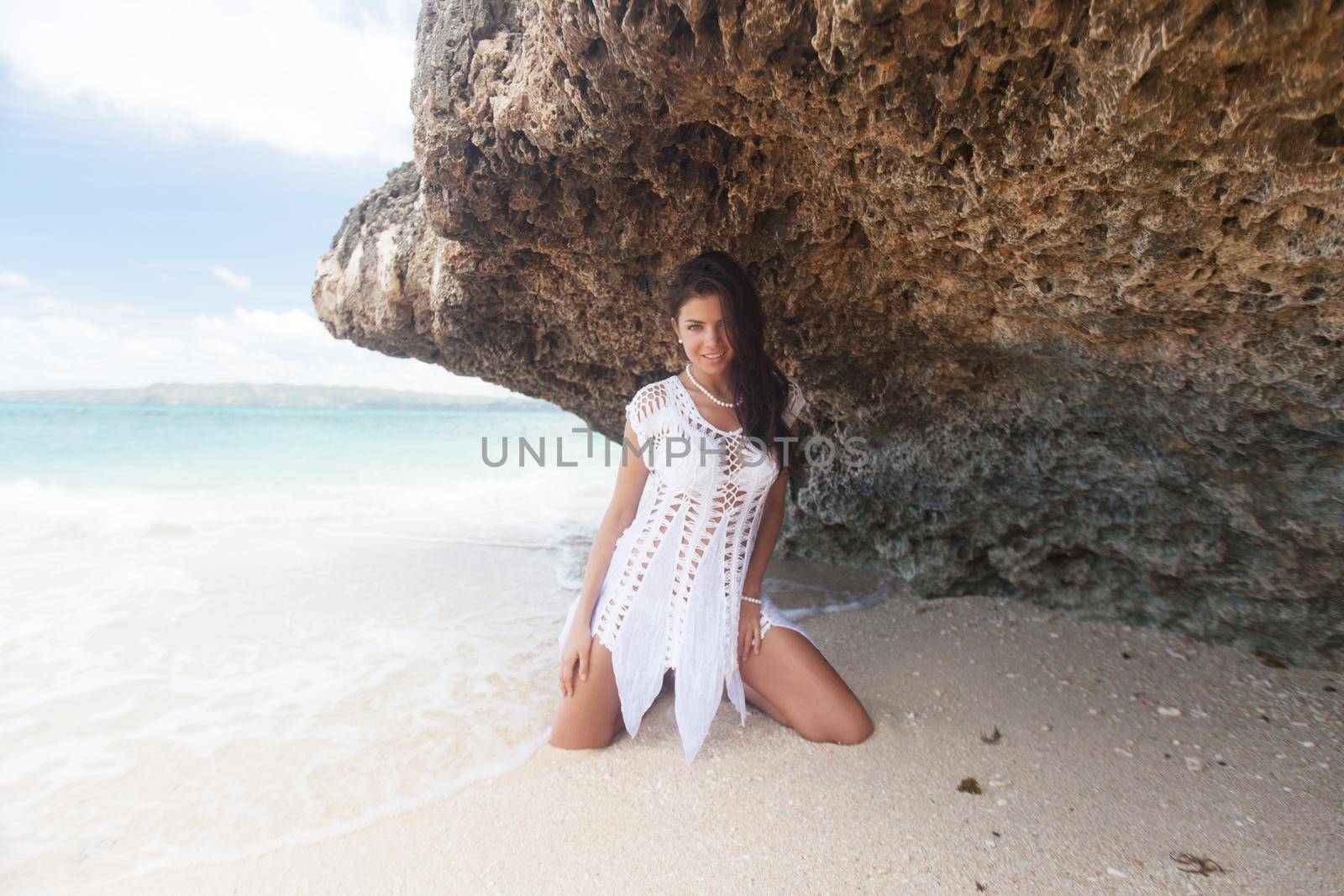 Girl in white dress posing on sea beach near limestone rock in Thailand