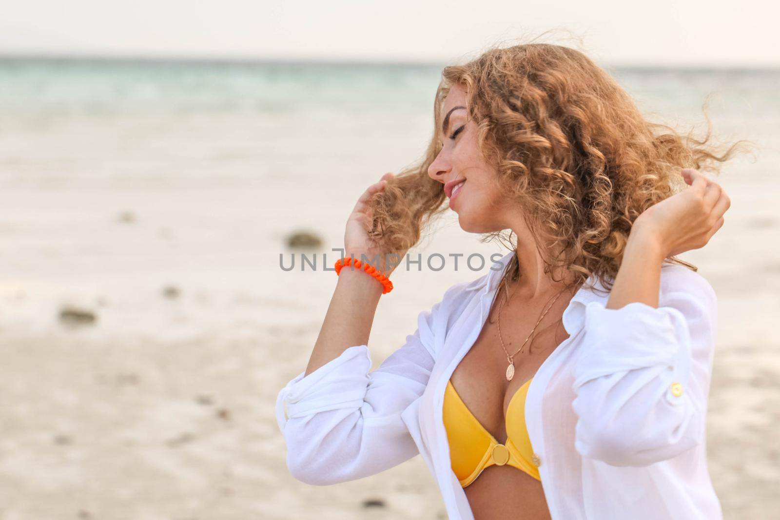 Beautiful woman with curly hair in bikini and white shirt enjoy summer vacation at tropical beach