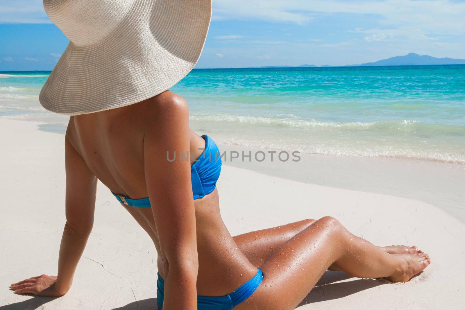 Woman in big sun hat sitting on beach by the sea side view