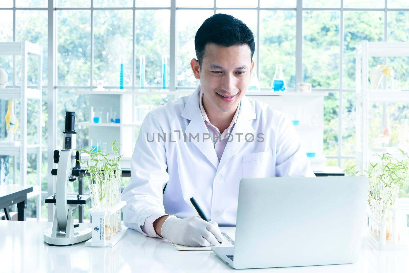 Asian researchers in white coats The concept of working in a scientific laboratory Using a laptop to find information And write down in the test results book Or making a report in a science laboratory