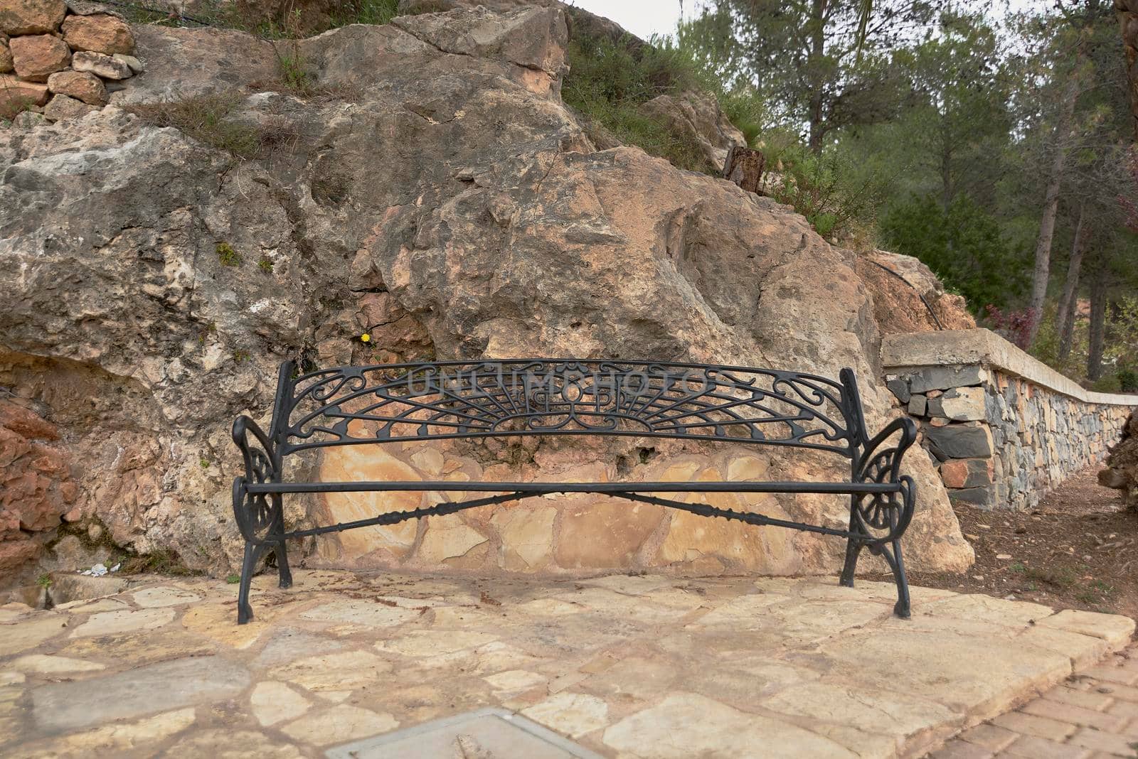Forged iron bench in the mountains. Large stones, yellow flower, pine trees, vegetation, solitary,