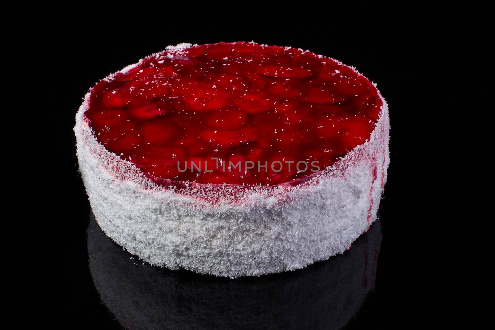 Big cake in coconut shavings with strawberries in jelly on a black background
