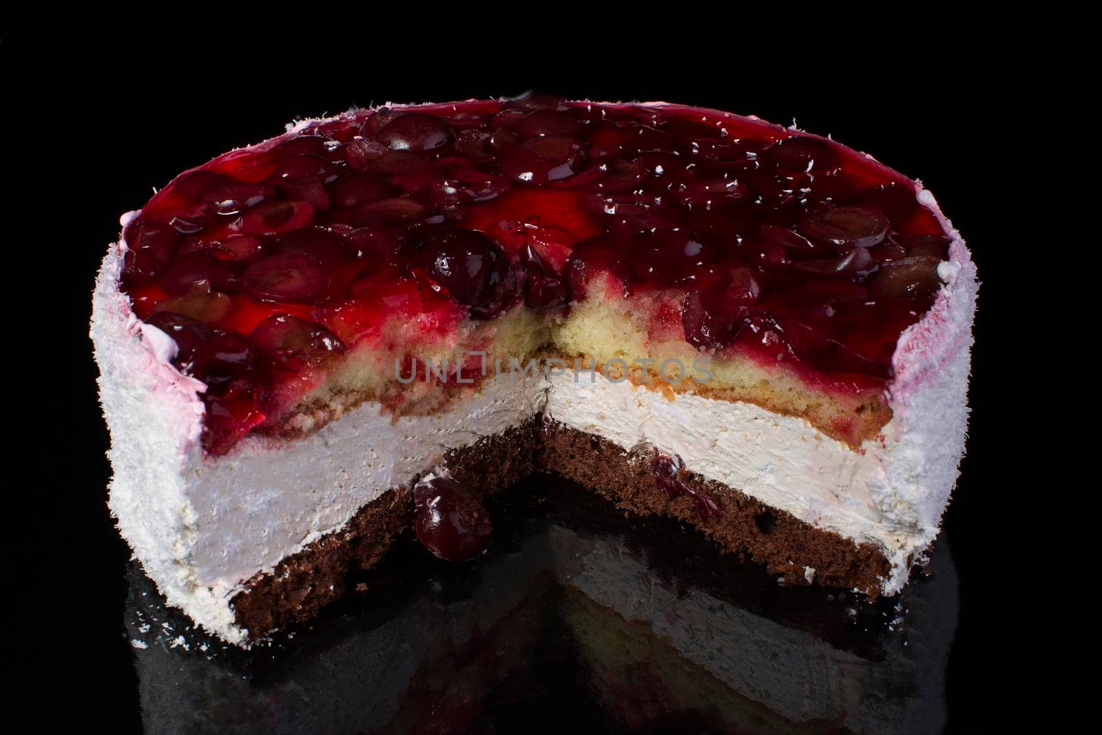 Piece of a large cake in coconut shavings with a cherry in jelly on a black background