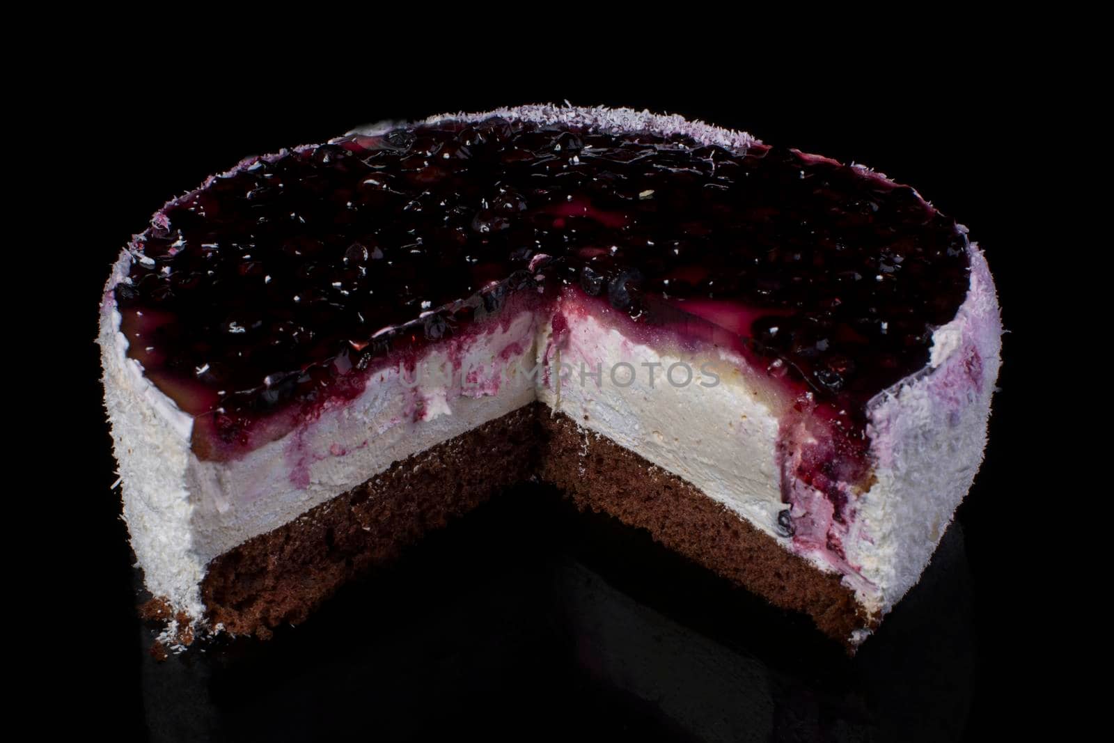 Piece of cake with coconut shavings and currant in jelly on a black background