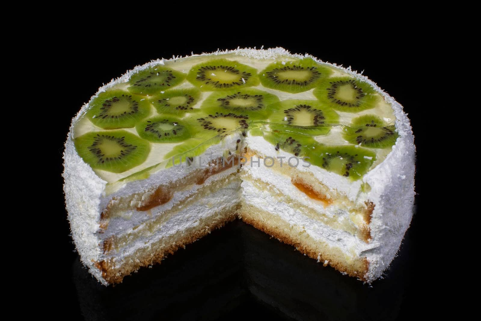 Cut off piece of white festive cake with kiwi and coconut shavings on a black background