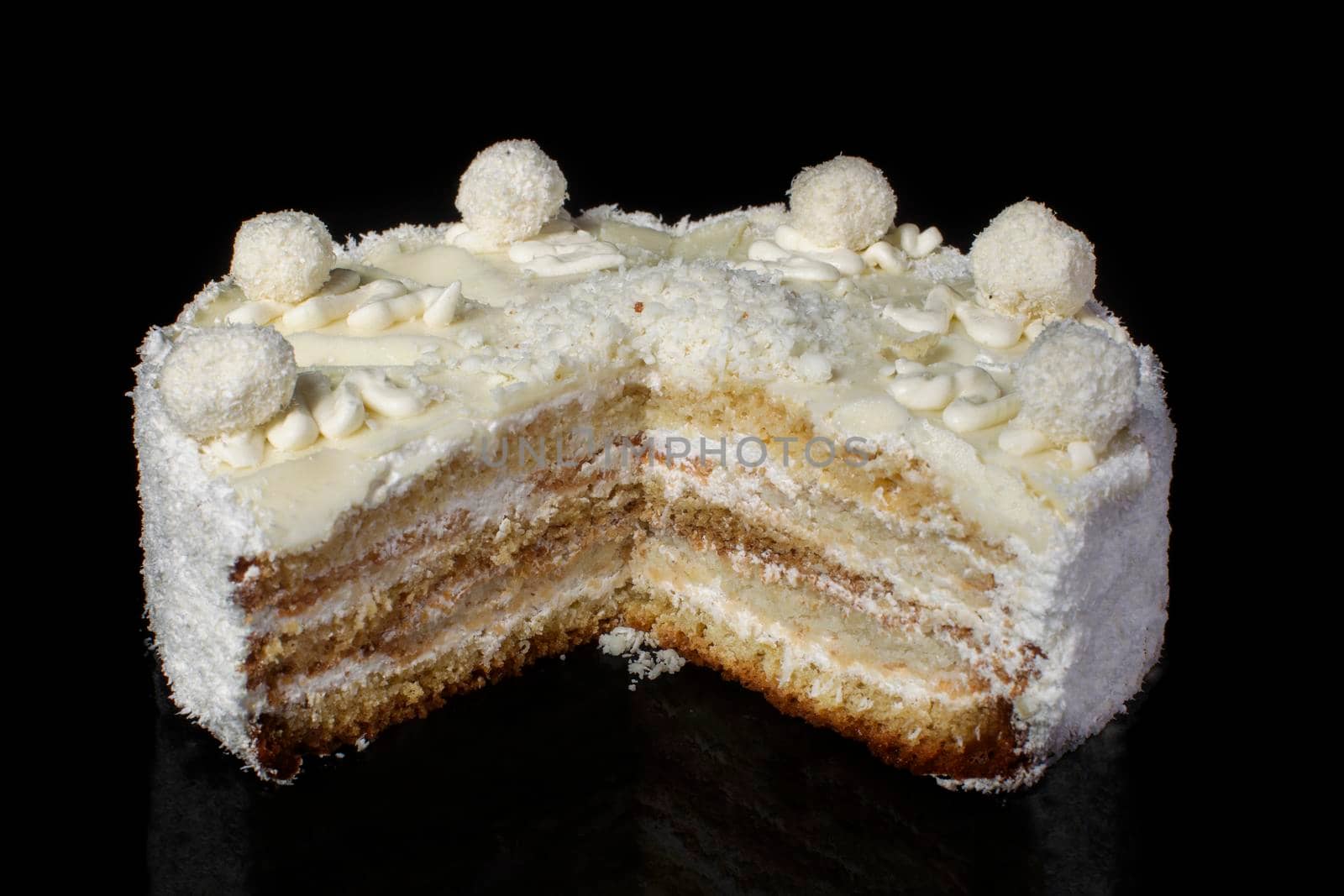 Cut off piece of white cake close-up with coconut shaving on a black background