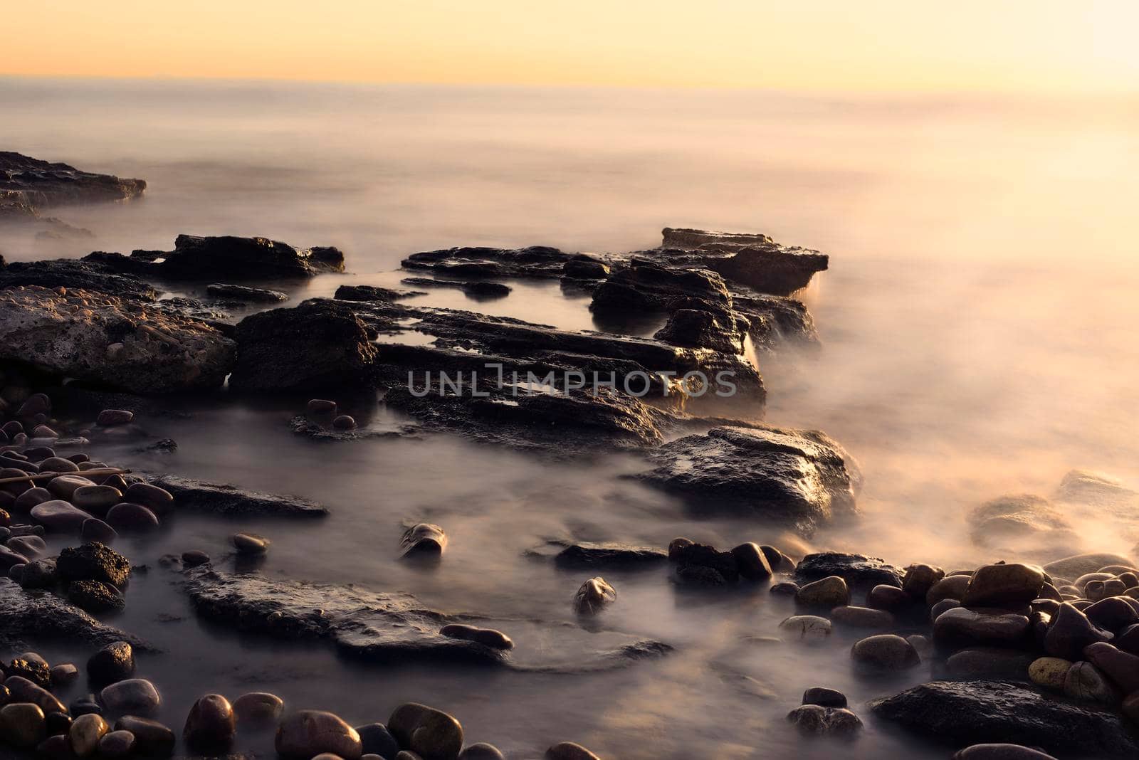 Sunrise on the rocky beach, long exposure, water silk effect