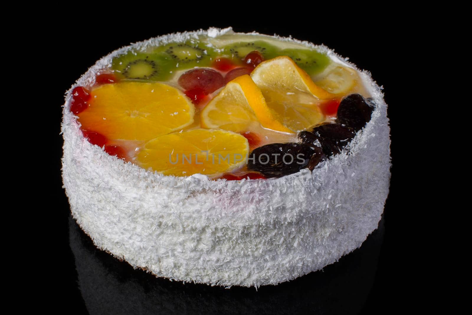 Beautiful fruit cake with orange kiwi gooseberries sprinkled with coconut shavings on a dark background