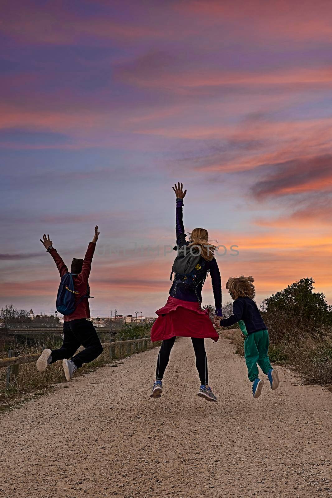 Young blonde woman with two children jumping. Caucasian, sportswear, blue sky , lifestyle, happy, orange sunset