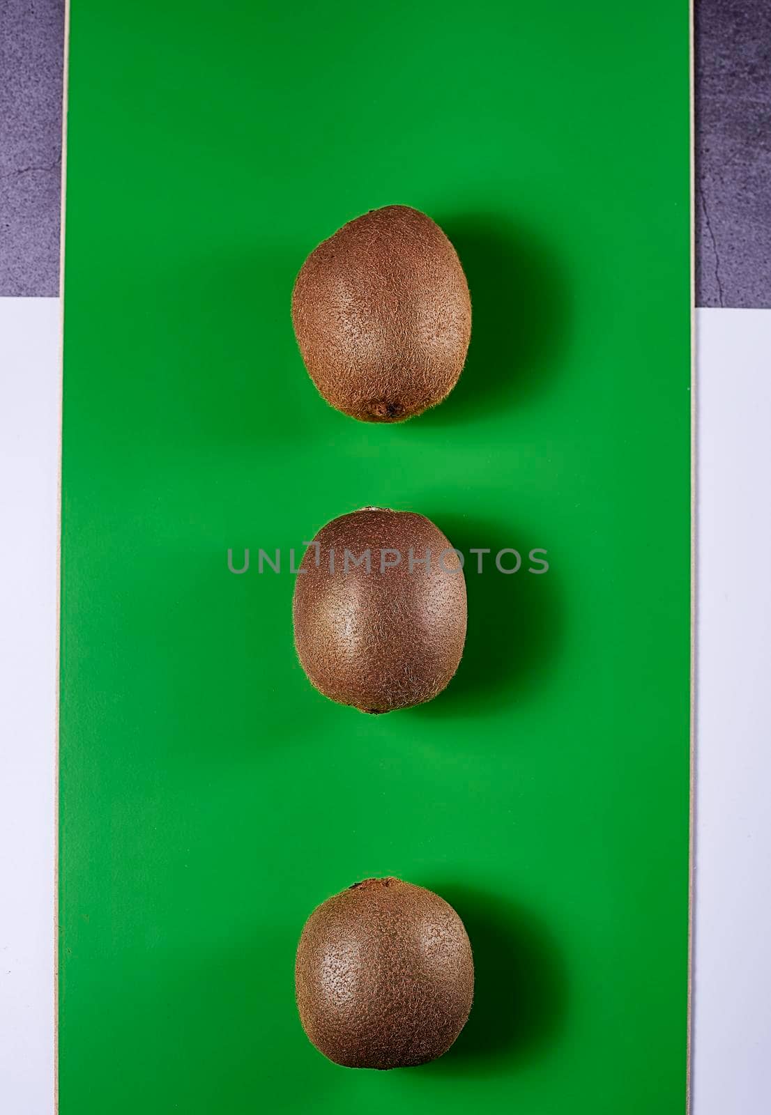 Three kiwis on green background, wood, white background and stone, zenithal view