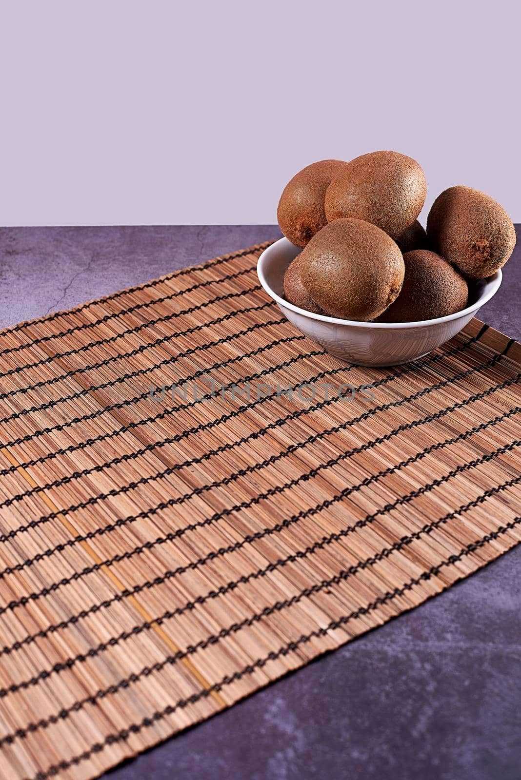 Kiwis in a bowl on a reed mat, stone floor and white background