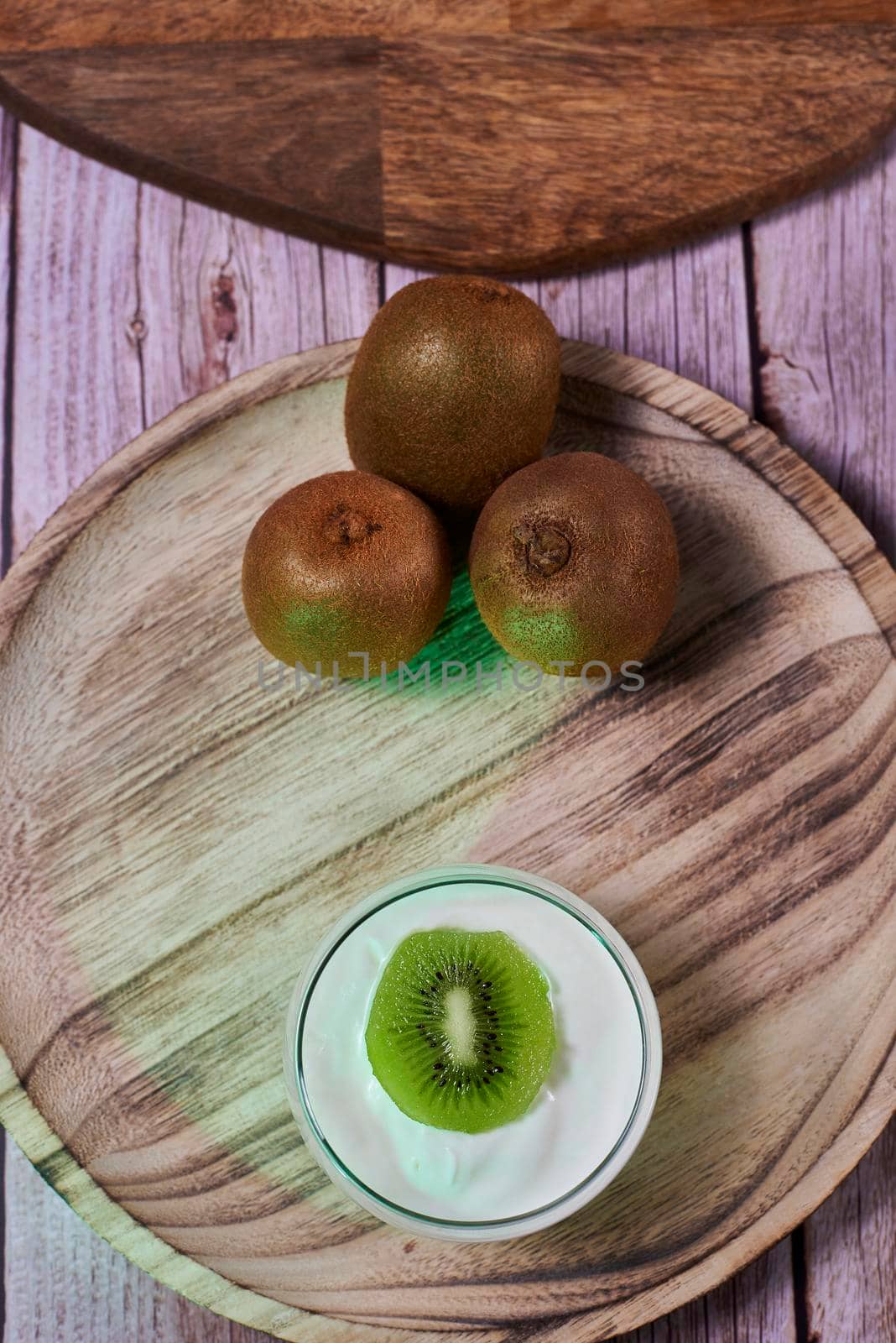 Yoghurt glass on wooden plate with kiwis. three kiwis, wooden floor and wooden tray.