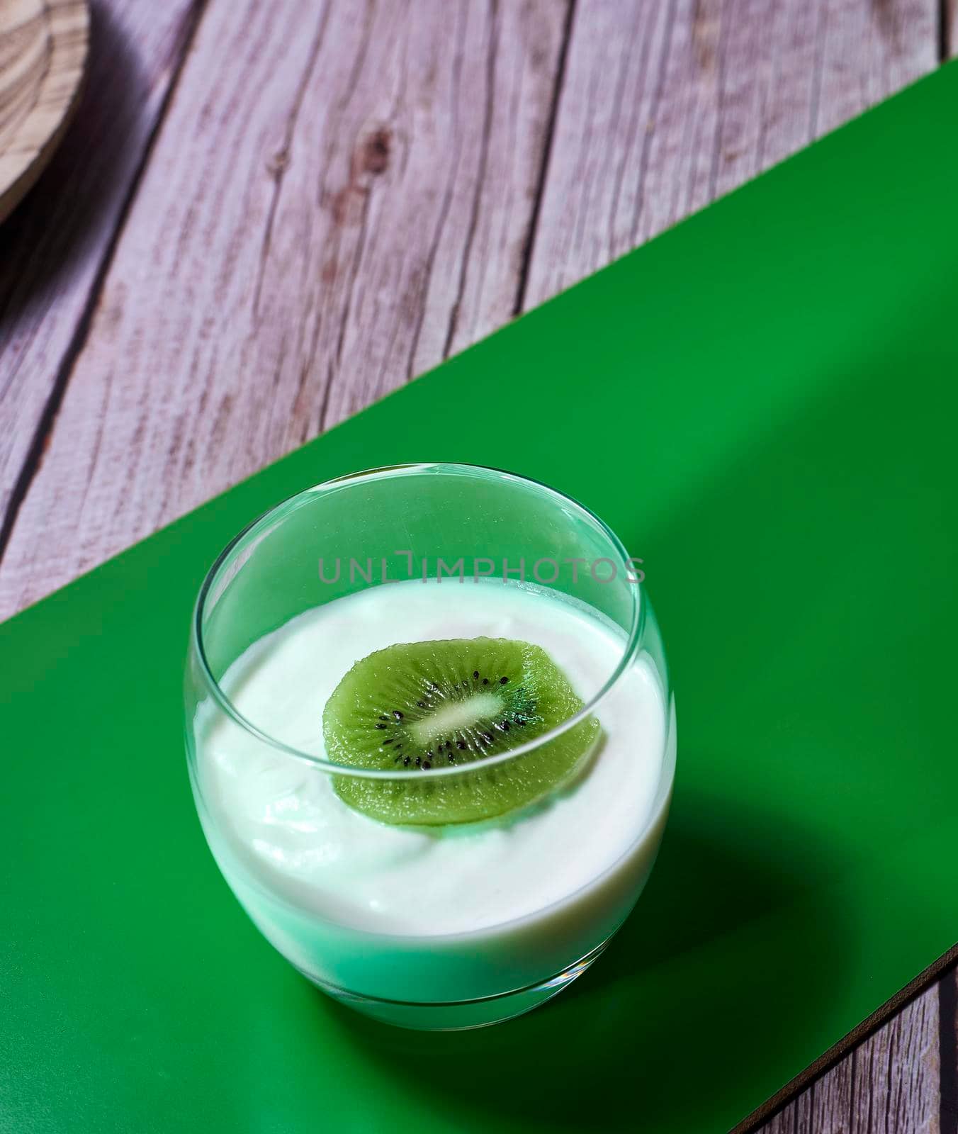 Glass of yoghurt with a sliced kiwi. Diagonal green wooden board, wooden planks
