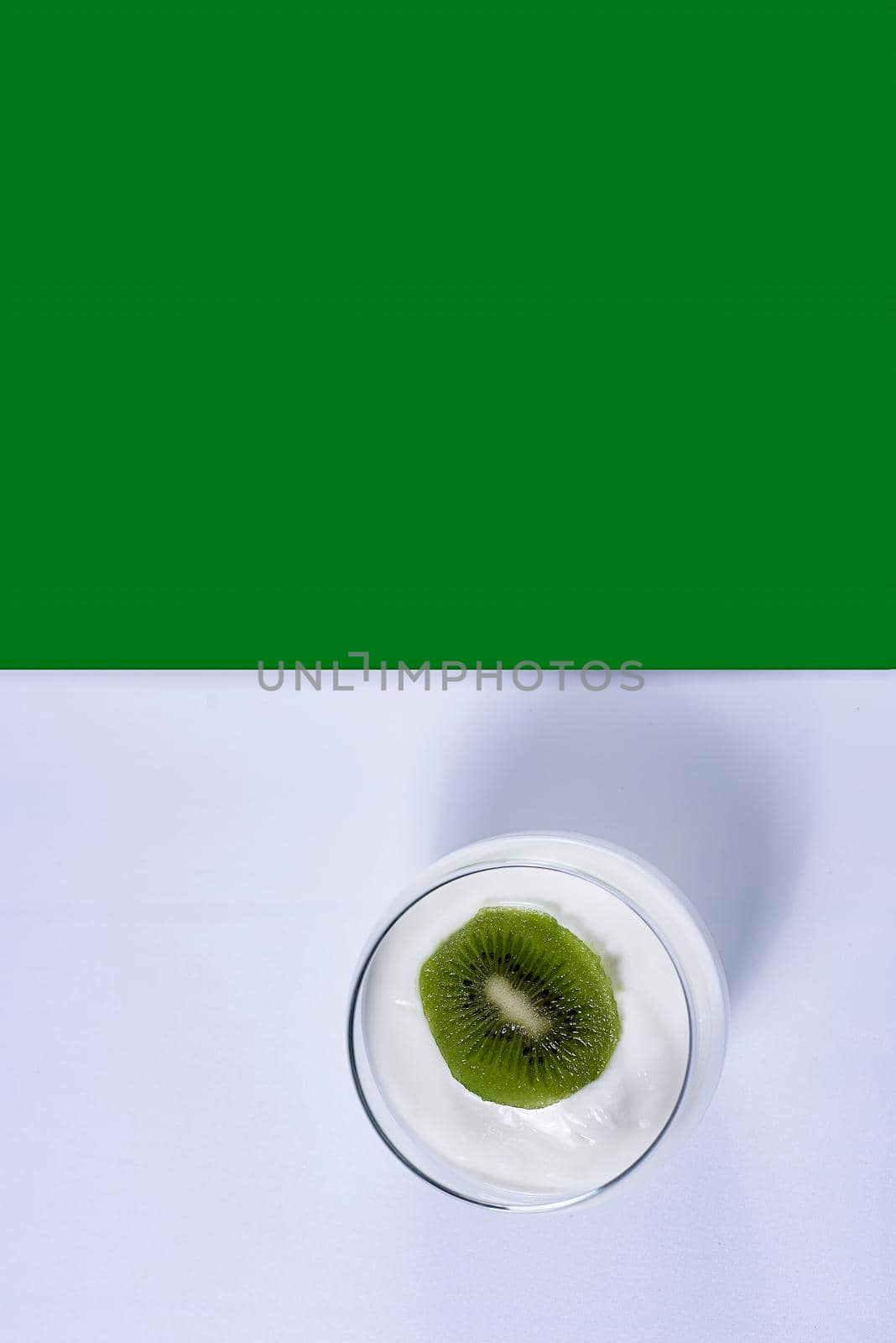 Glass of yoghurt with a sliced kiwi. White and green background, symmetrical, vertical.down