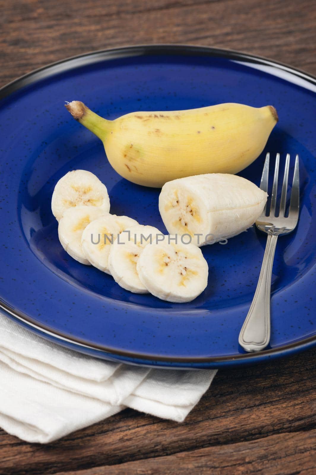 peeled and sliced cultivated banana on blue plate, healthy eating concept