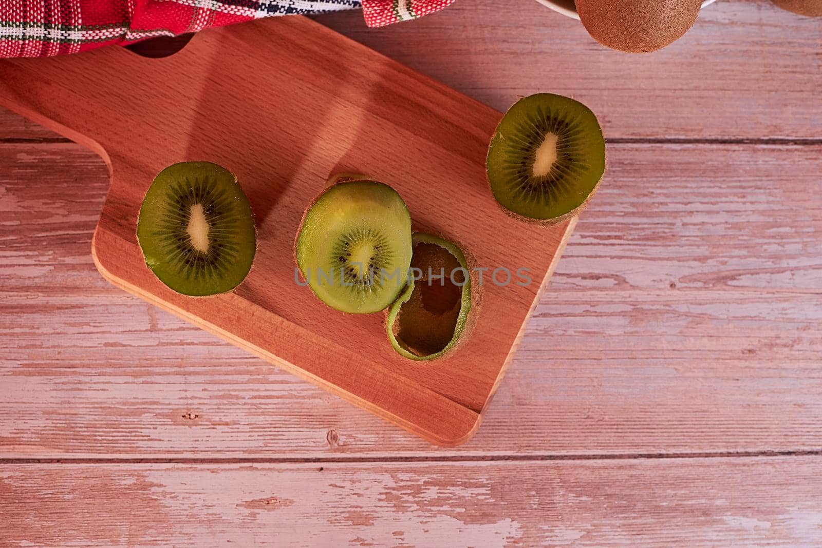 Cut kiwis on wooden board. wooden floor, zenithal view, red and white cloth, empty space.