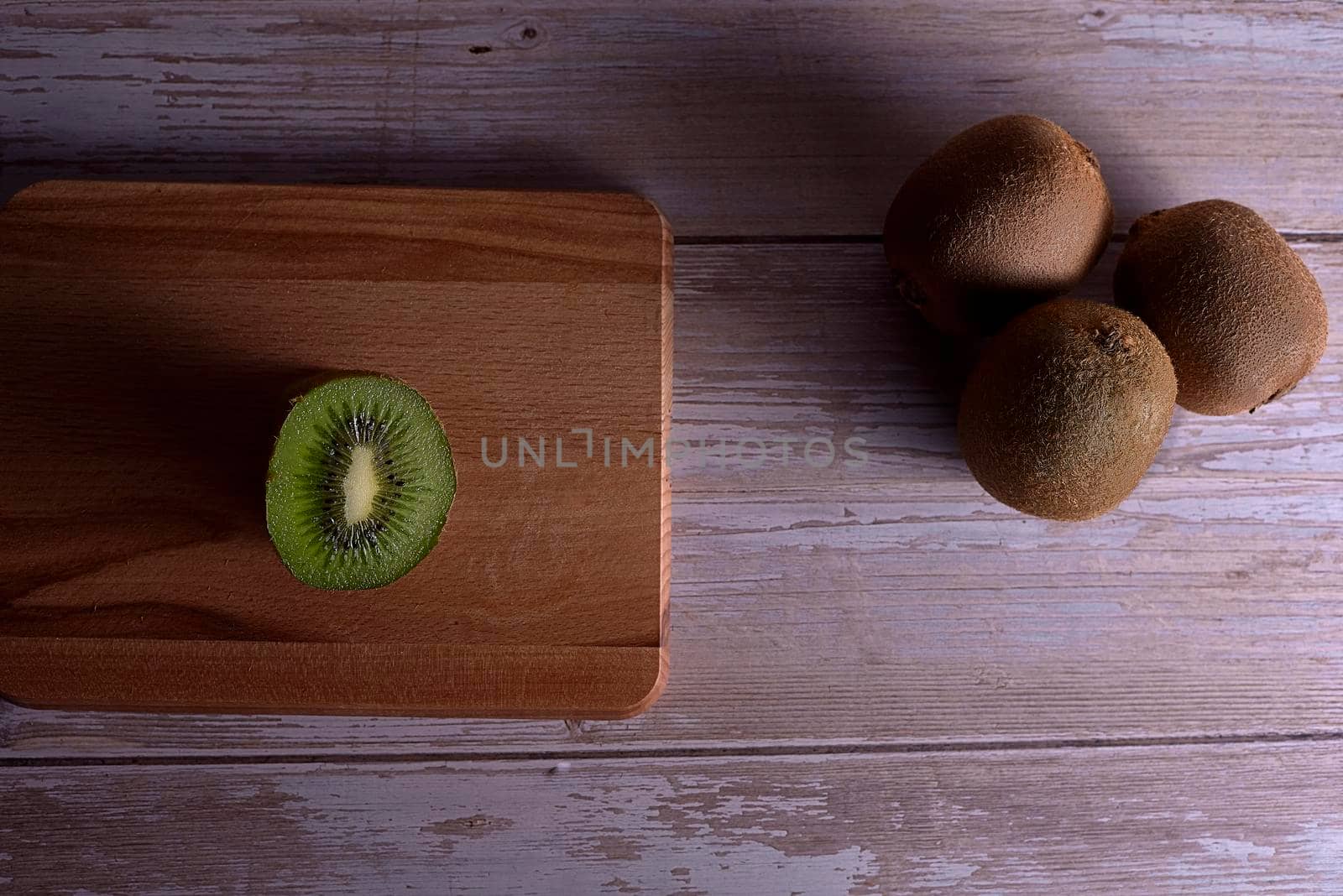 Kiwifruit cut on a wooden board. Three uncut kiwis on wooden boards, top view.