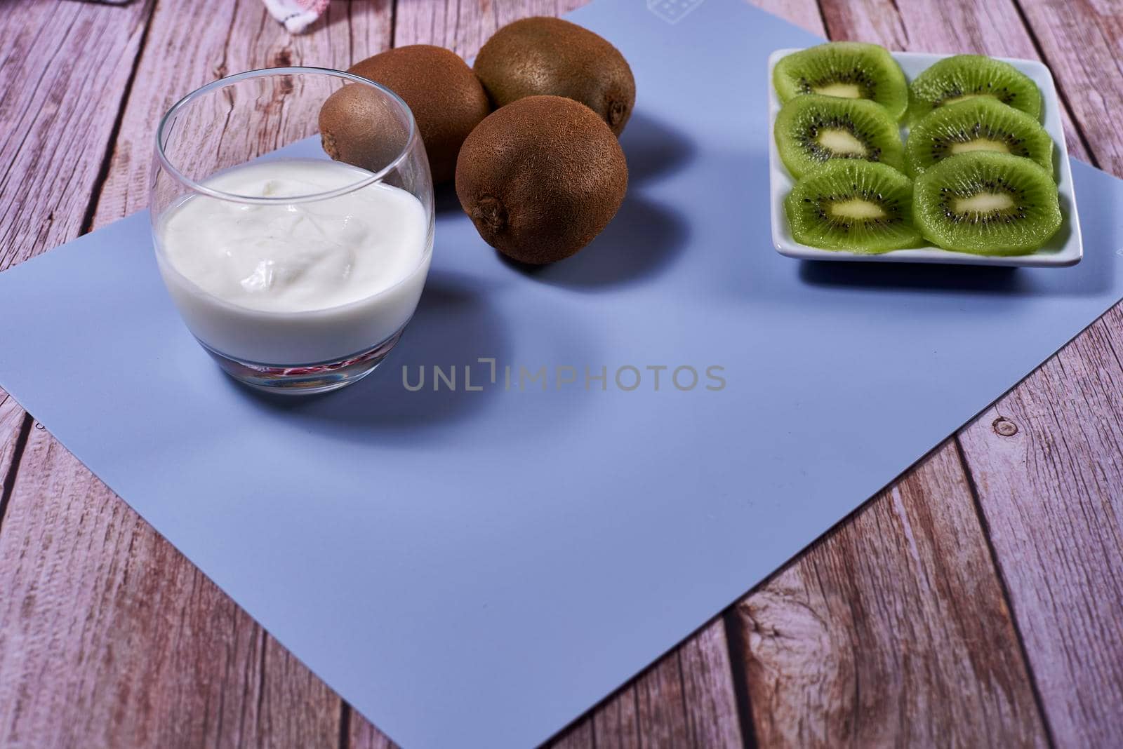 Glass of yoghurt with kiwis. Wooden floor, red and white kitchen towel, checkered, blue tablecloth.