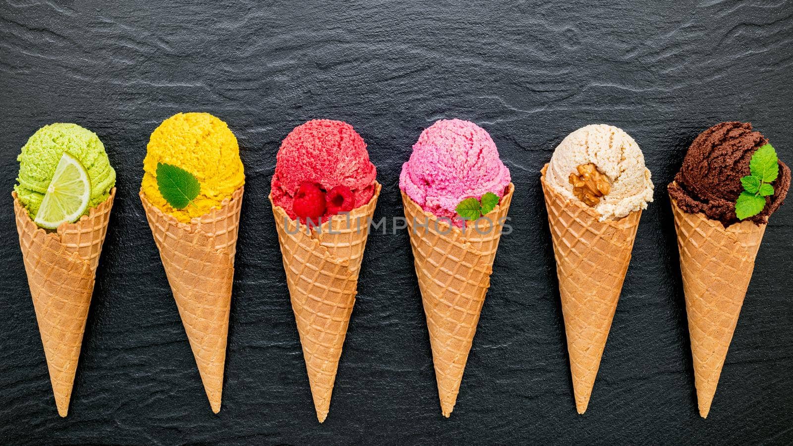 Various of ice cream flavor in cones blueberry ,lime ,pistachio ,almond ,orange ,chocolate ,vanilla and coffee set up on dark stone background . Summer and Sweet menu concept. by kerdkanno