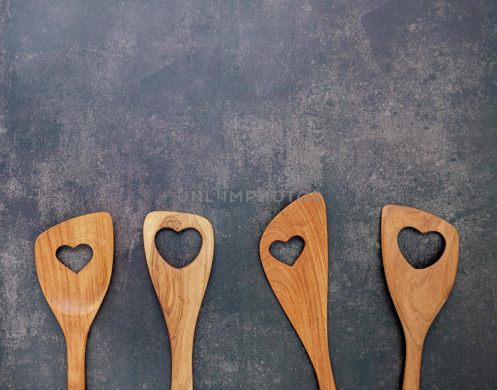 Various heart shape of wooden cooking utensils. Wooden spoons and wooden spatula on dark concrete background with flat lay and copy space.