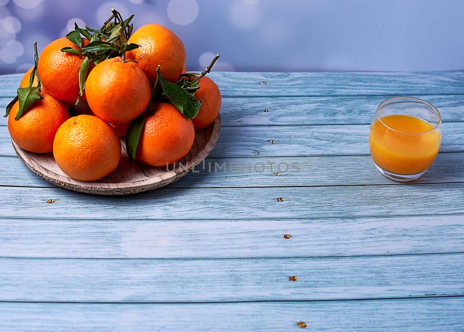Glass of orange juice with various oranges on wooden plate on wooden floor and bright background, empty space