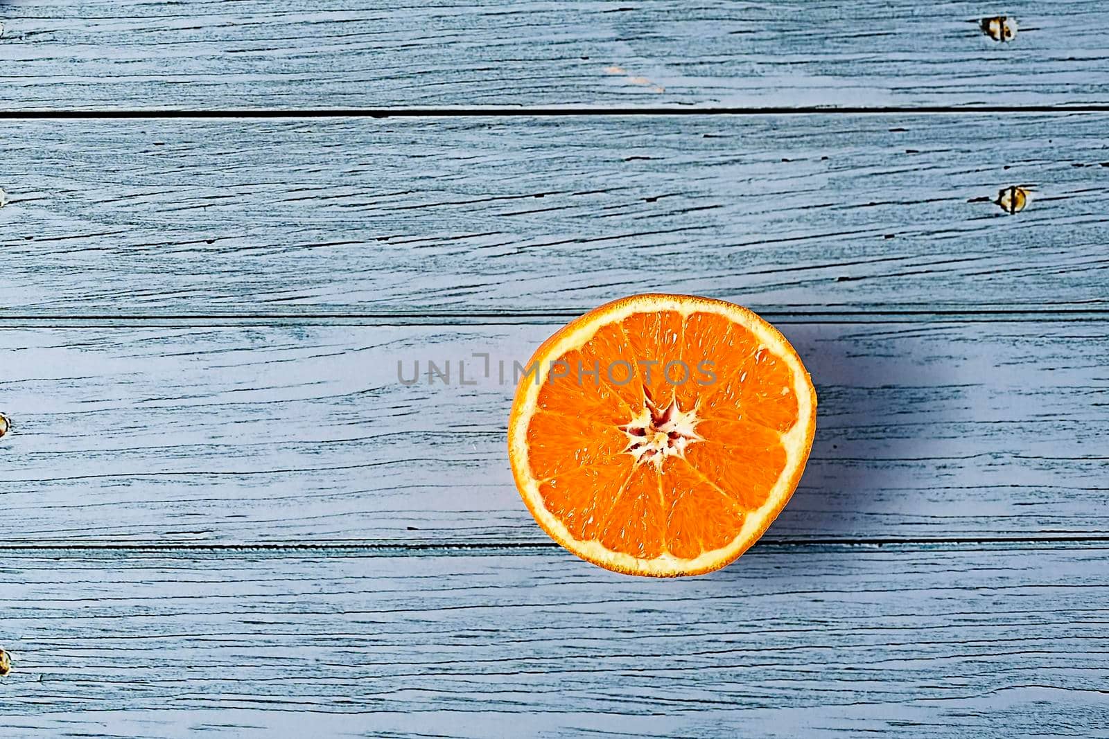 Half orange on wooden floor with nails, blank space, overhead view