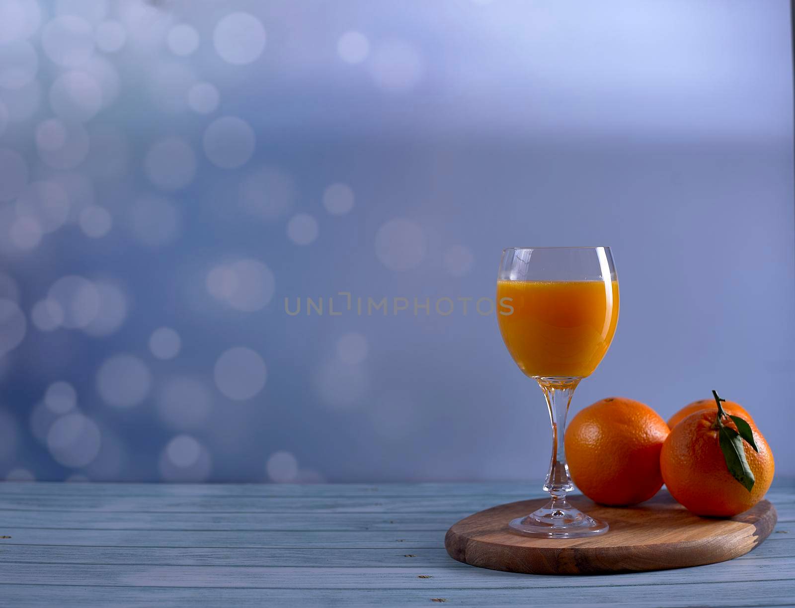 Glass of orange juice with various oranges on wooden table on bright background and wooden floor, free space, front view