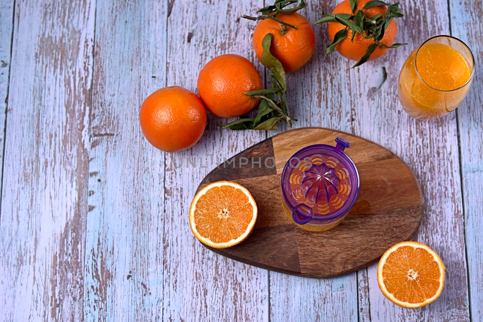 Glass of orange juice with glass squeezer on wooden table, several oranges on wooden floor, overhead view