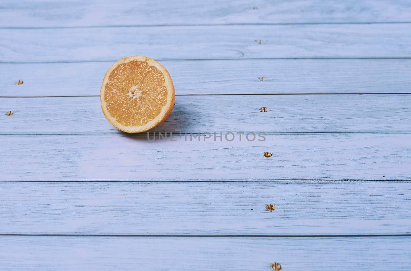 Half orange on light wooden floor with nails, overhead view