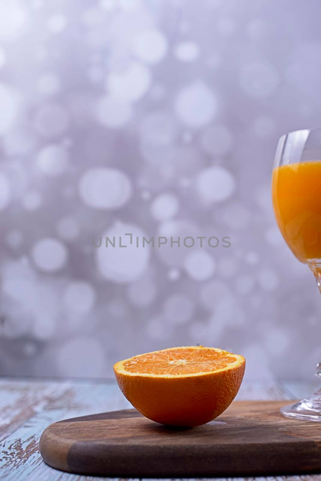 Glass of orange juice cut on wooden table bright background, front view, half orange