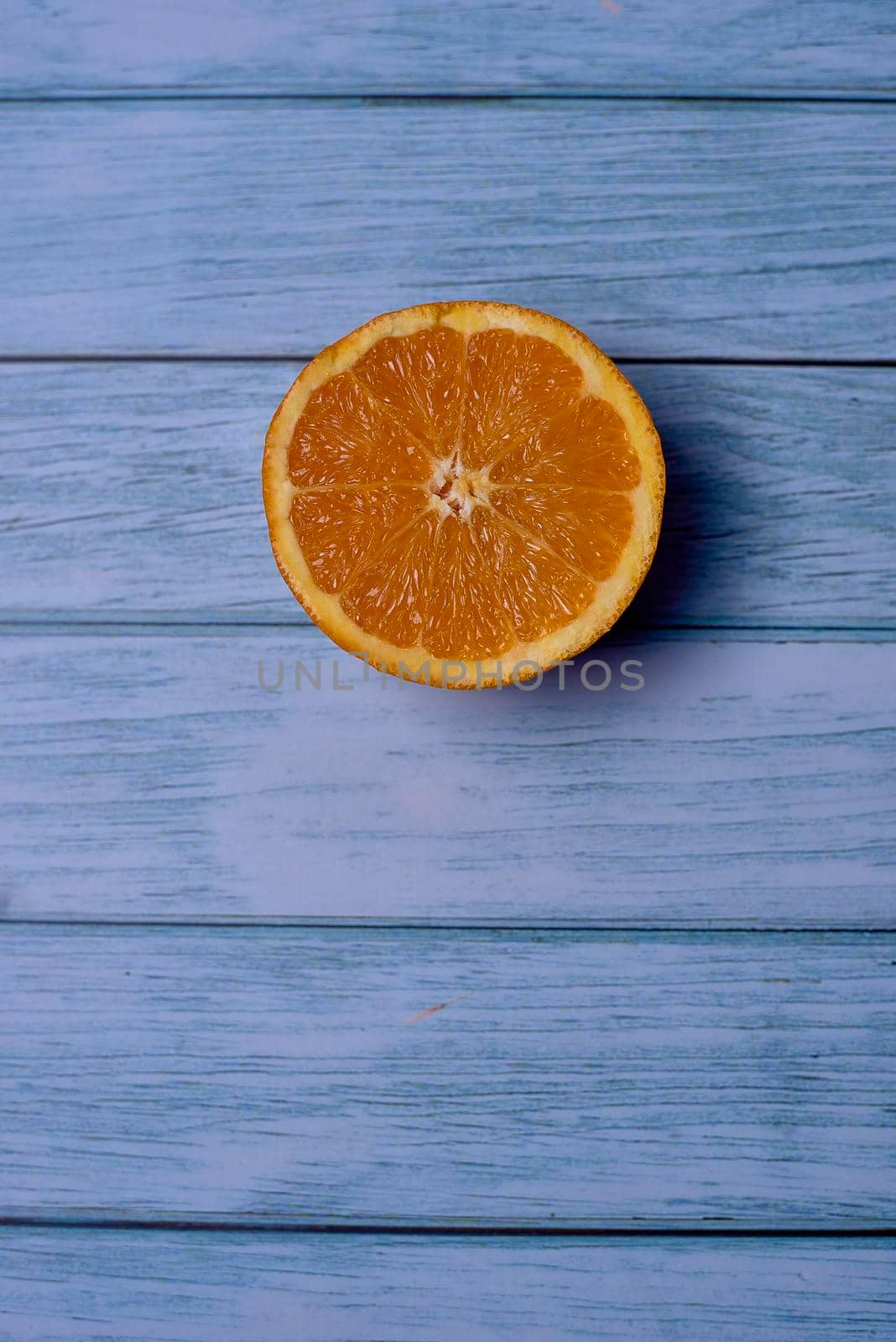 Half orange on light wooden floor with nails, overhead view